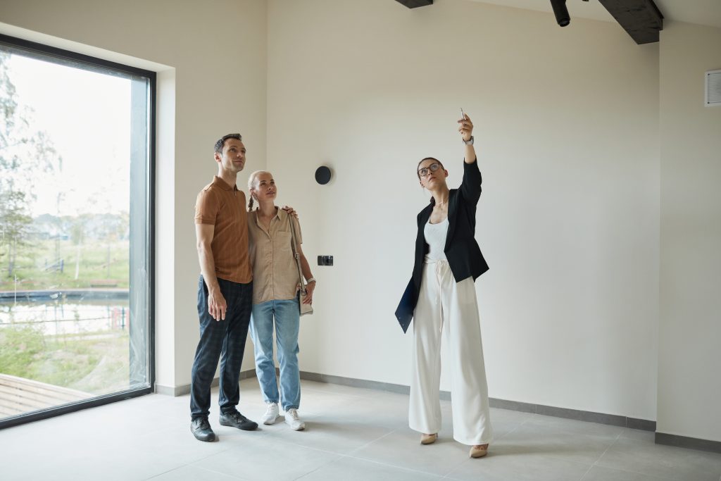 Ganzkörperporträt einer Immobilienmaklerin, die einem jungen Paar, das eine neue Immobilie kaufen möchte, eine Wohnung zeigt, Textfeld