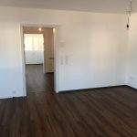 Wohnraum mit dunklem Parkettboden und einer Glastür die zu weiteren Räumen führt.